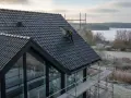 Arbetare på taket av ett modernt hus med svarta takpannor. Vindskivor huset är i fokus. Vinterlandskap med isig sjö i bakgrunden.