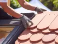 Händer med handskar lägger nya takpannor. Ett takprojekt för att renovera takpannor pågår.