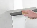 Handen spacklar en vägg med en bred spackel. Arbetet med att kapa gipsskiva kan nu fortsätta.