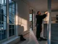 Man arbetar med eldstad inomhus. Solen lyser in genom stora fönster och skapar långa skuggor.