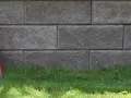 Två staplar takpannor, en svart och en röd, lutar mot en mur av grå betongblock. Undrar vad kostar takpannor?