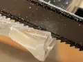 Sågtänder skär genom ett tjockt, klart material. Små bitar av materialet flyger iväg när man kapa plexiglas.