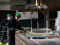 Två arbetare i skyddsutrustning hanterar metall som doppas i ett bad. Processen för varmförzinkning pris kan variera beroende på material och storlek.