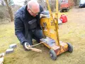 Man klipper marksten med en gul maskin. Han mäter med tumstocken för att få rätt längd.