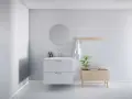 Minimalistiskt badrum med vitt kommod, rund spegel och trädetaljer. En bra utgångspunkt för att fundera på vad kostar det att renovera ett litet badrum.