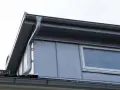 Grå takränna leder vatten från en stor takkupa med fönster.