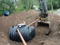 Grävmaskin installerar enskilt avlopp. En stor plasttank placeras i marken, vilket är en del av enskilt avlopp kostnad.