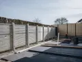 Byggarbetsplats med nya plintar och ett staket som håller på att monteras. Material ligger utspritt på marken.
