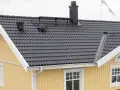 Taket har mörka takpannor, en svart skorsten och en svensk flagga. Vindskiveplåt montering syns längs takkanten.