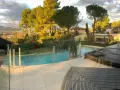 Solnedgång över en pool med trall runt om. Vackert landskap med träd och berg i bakgrunden.