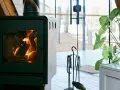 En modern kamin med sprakande eld. Bredvid står en växt och en uppsättning verktyg, allt enligt eldstadsplan regler för säkerhet.