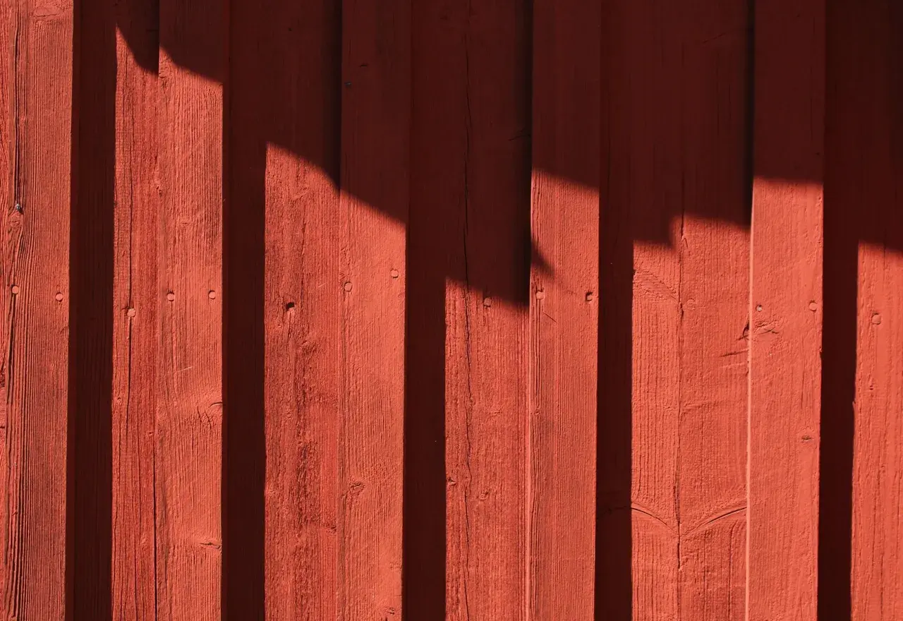 Röda träpaneler med skuggor som faller. Kanske är det dags att måla huset igen?