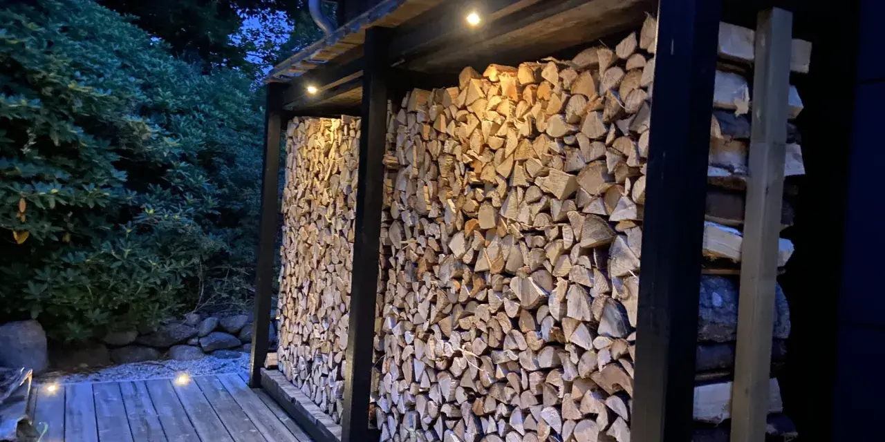 En vedbod är färdig att bygga, fylld med ved och belyst av små lampor.