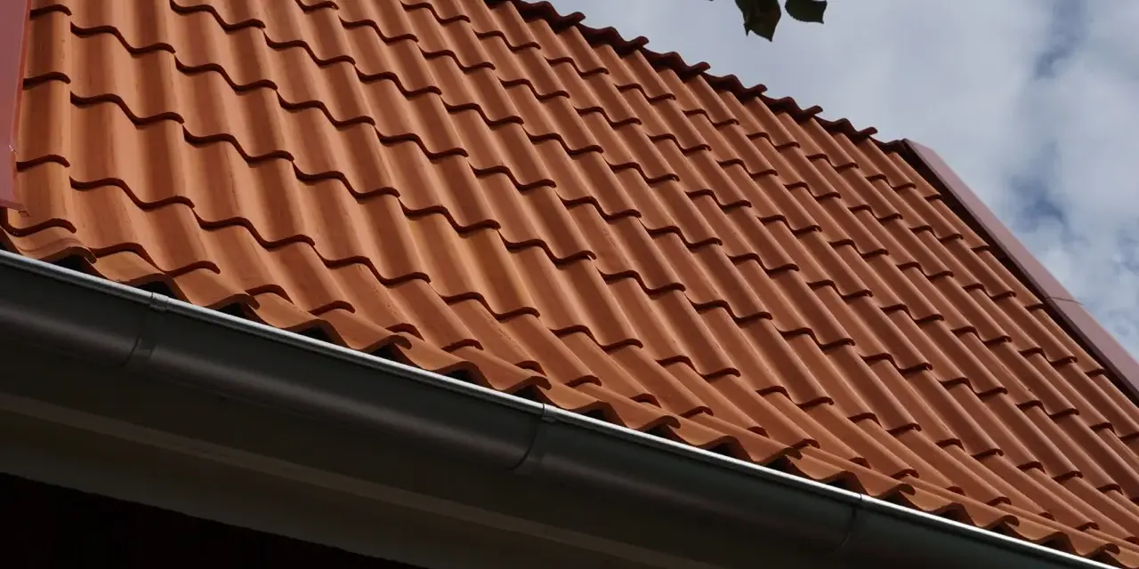 Rött tegeltak med rännsten. Taket har en minimal taklutning för betongpannor, vilket ger ett stilrent utseende.