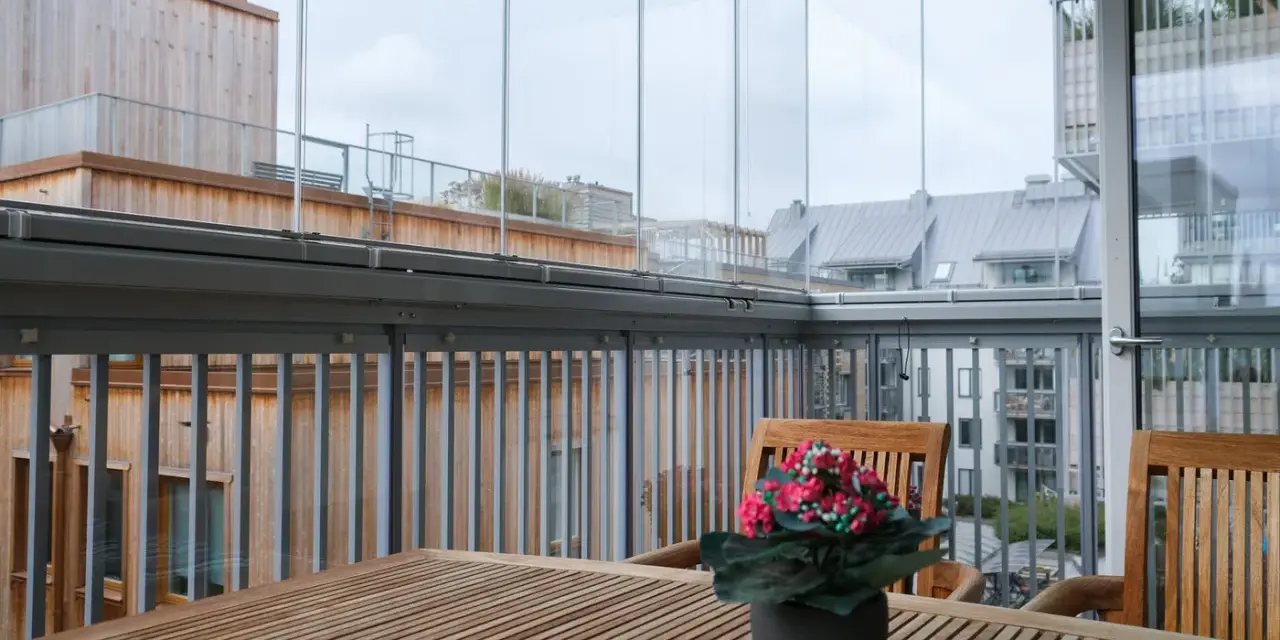 Träbord och stolar på en inglasad balkong med utsikt över stadens tak. Tänk på inglasad balkong pris för din egen dröm.