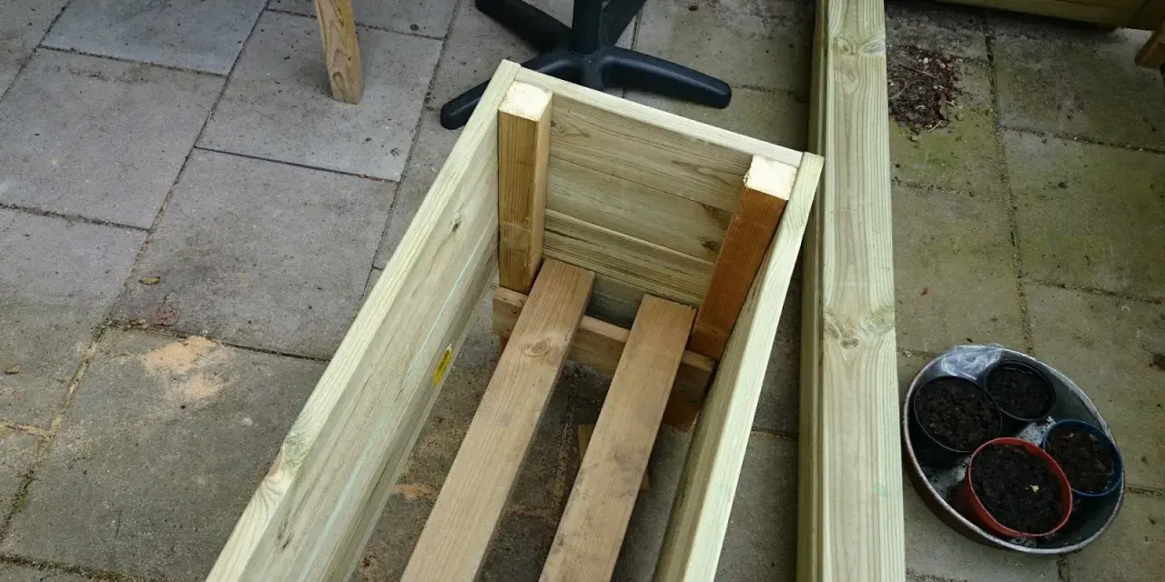 Påbörjat projekt att bygga blomlåda av tryckimpregnerat virke. Några krukor med jord står redo.