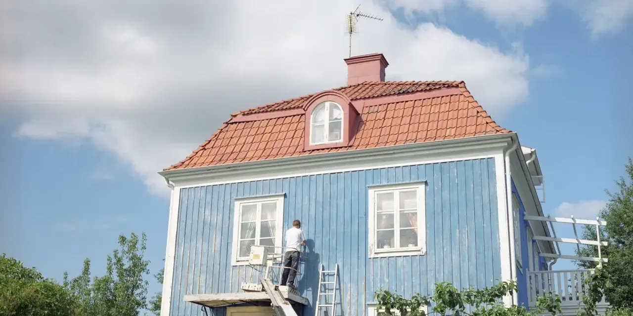 Man målar om en blå träfasad från en lift. En dropplist fasad skyddar mot regn.