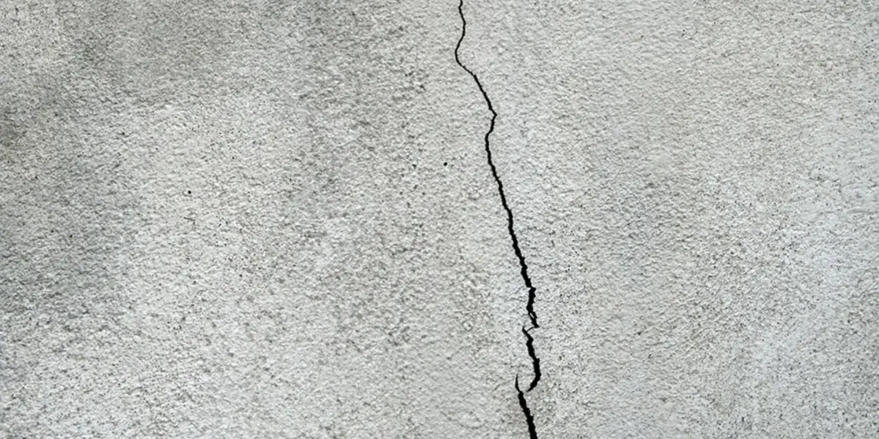En spricka löper genom en grov, grå putsad fasad. Dags att putsa fasaden för att laga skadan.