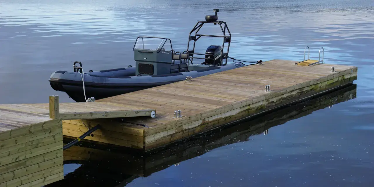 En grå RIB-båt ligger förtöjd vid en nybyggd flytbrygga. Perfekt för att bygga flytbrygga och njuta av vattnet.