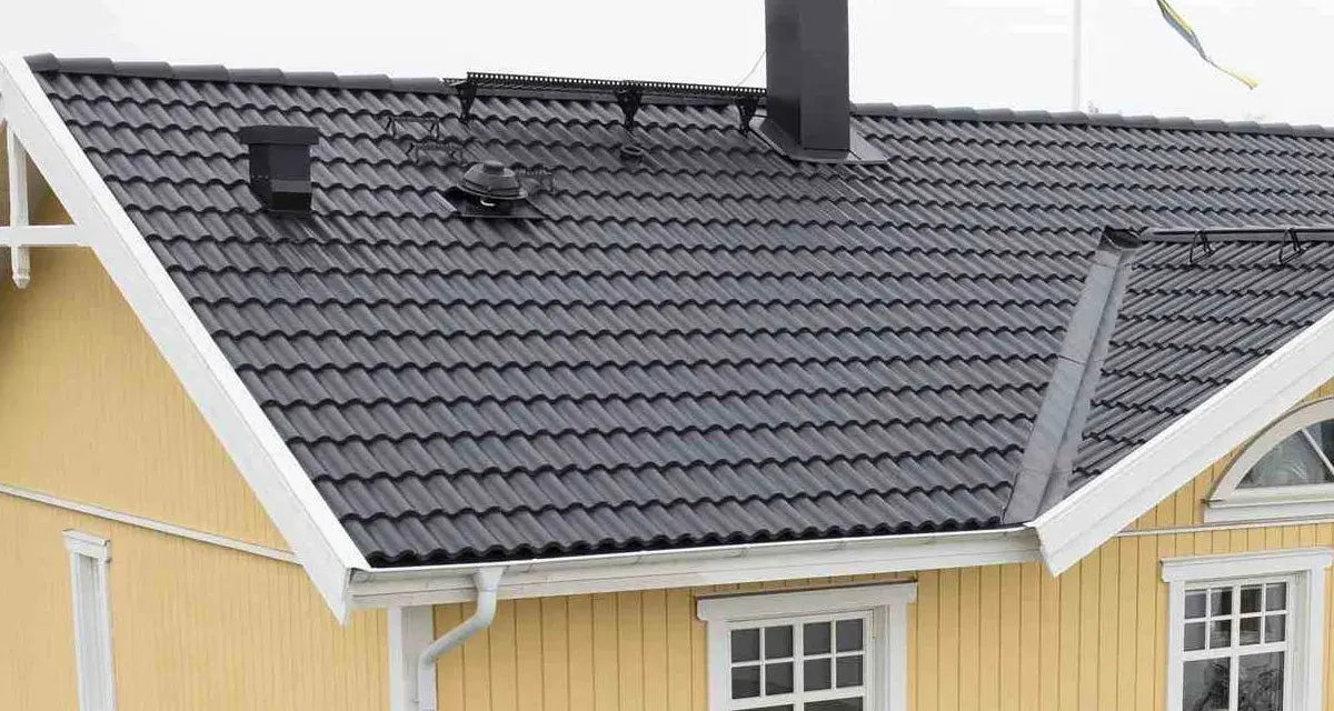 Taket har mörka takpannor, en svart skorsten och en svensk flagga. Vindskiveplåt montering syns längs takkanten.