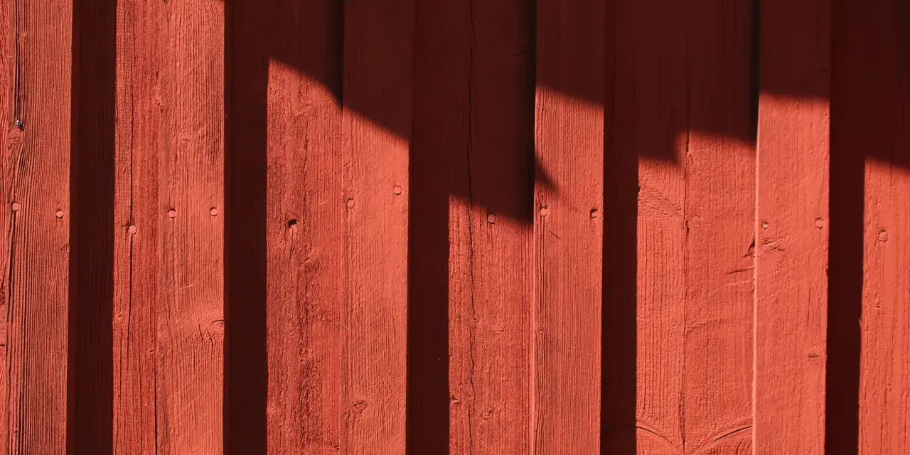 Röda träpaneler med skuggor som faller. Kanske är det dags att måla huset igen?