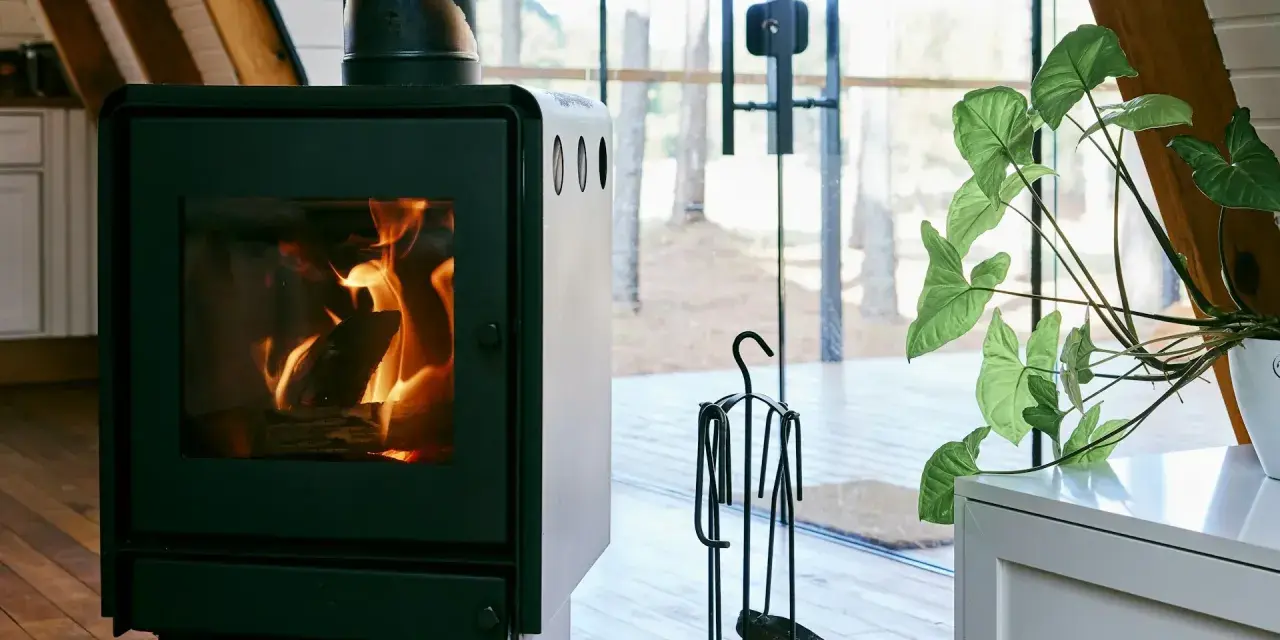 En modern kamin med sprakande eld. Bredvid står en växt och en uppsättning verktyg, allt enligt eldstadsplan regler för säkerhet.