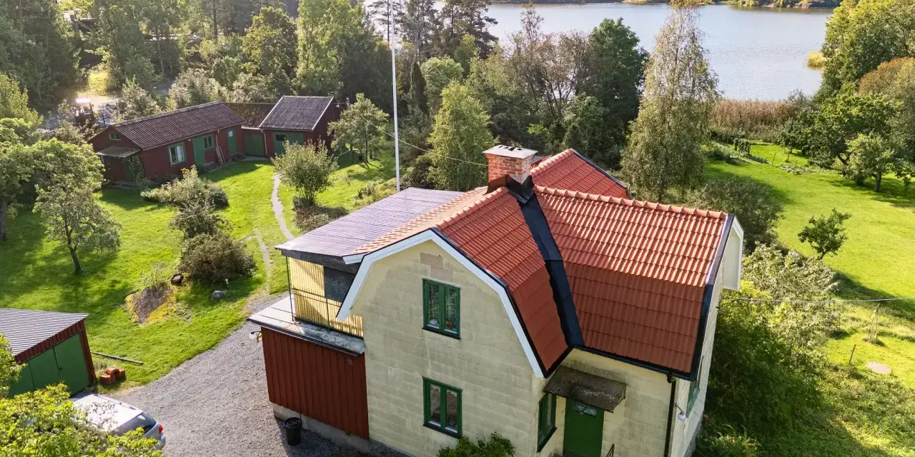 Gult hus med tegeltak vid en sjö. En takrenovering kostnad kan vara en bra investering för att skydda huset.