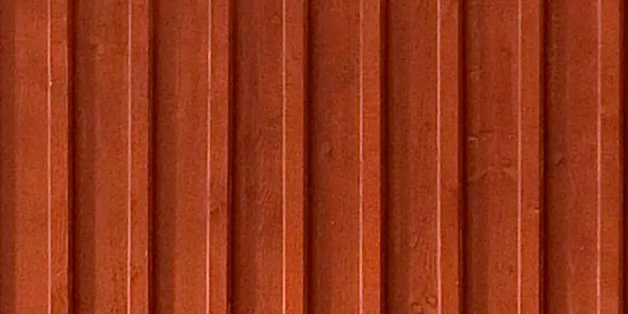 Detaljbild av en rödbrun, gammaldags lockpanel i trä. Panelen har vertikala spår och ger en känsla av traditionellt svenskt byggnadssätt.