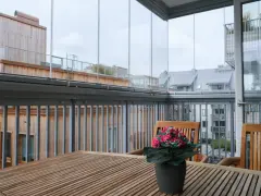 Träbord och stolar på en inglasad balkong med utsikt över stadens tak. Tänk på inglasad balkong pris för din egen dröm.