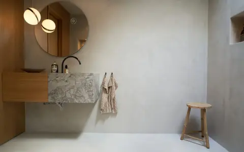 Modernt badrum med handfat i marmor och trä, rund spegel och två lampor. Tänk på microcement badrum pris för en liknande stil.