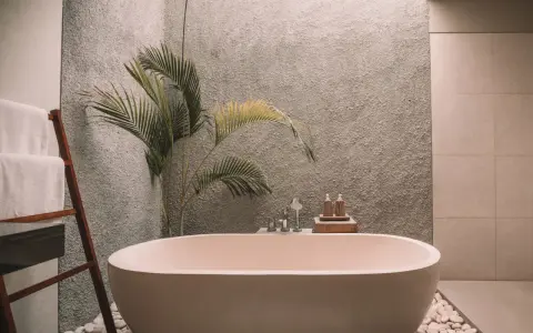 Ett modernt badrum med ett fristående badkar. En stege med vita handdukar står bredvid. En palm växer bakom badkaret. Kanske dags att måla badkar för en ny look?