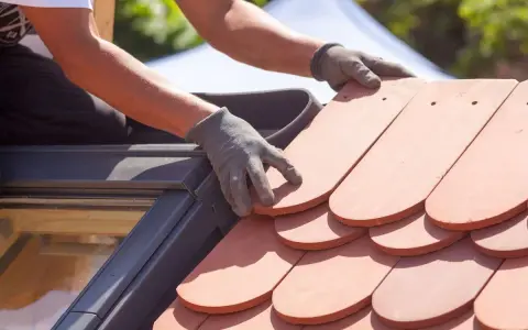 Händer med handskar lägger nya takpannor. Ett takprojekt för att renovera takpannor pågår.