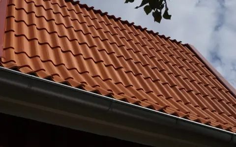 Rött tegeltak med rännsten. Taket har en minimal taklutning för betongpannor, vilket ger ett stilrent utseende.