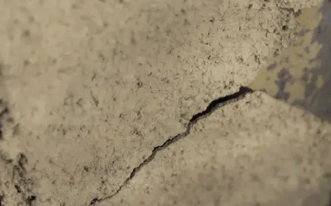 Detaljerad vy av sprucket putsbruk utomhus. Ytan är grov och ojämn med skuggor som framhäver sprickan.