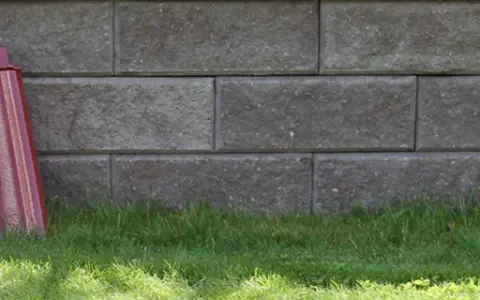 Två staplar takpannor, en svart och en röd, lutar mot en mur av grå betongblock. Undrar vad kostar takpannor?
