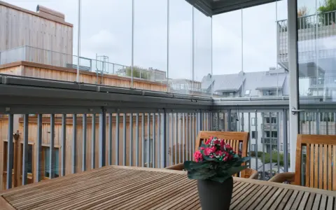 Träbord och stolar på en inglasad balkong med utsikt över stadens tak. Tänk på inglasad balkong pris för din egen dröm.