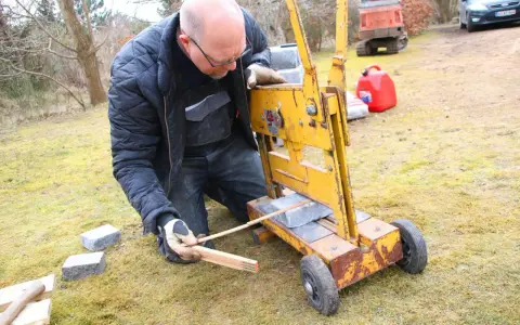 Man klipper marksten med en gul maskin. Han mäter med tumstocken för att få rätt längd.