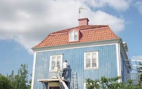 Man målar om en blå träfasad från en lift. En dropplist fasad skyddar mot regn.