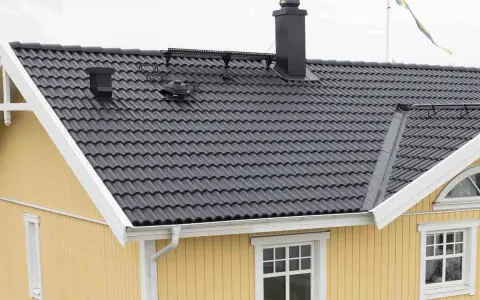 Taket har mörka takpannor, en svart skorsten och en svensk flagga. Vindskiveplåt montering syns längs takkanten.