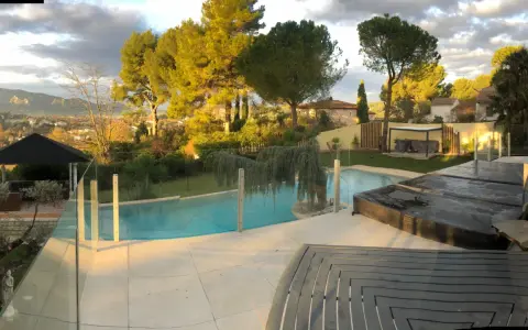 Solnedgång över en pool med trall runt om. Vackert landskap med träd och berg i bakgrunden.