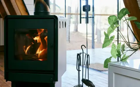 En modern kamin med sprakande eld. Bredvid står en växt och en uppsättning verktyg, allt enligt eldstadsplan regler för säkerhet.