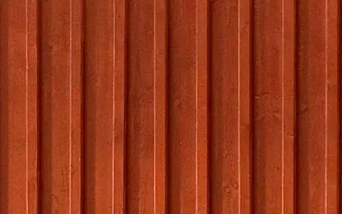Detaljbild av en rödbrun, gammaldags lockpanel i trä. Panelen har vertikala spår och ger en känsla av traditionellt svenskt byggnadssätt.