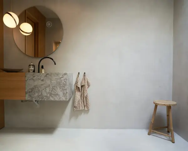 Modernt badrum med handfat i marmor och trä, rund spegel och två lampor. Tänk på microcement badrum pris för en liknande stil.
