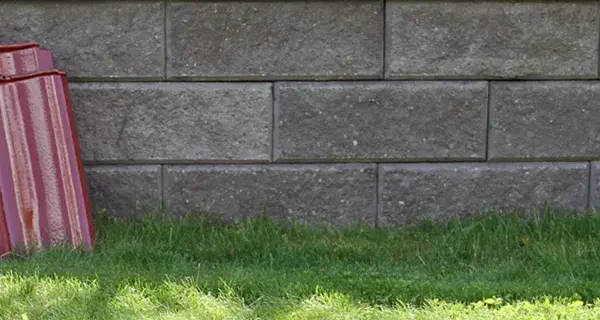 Två staplar takpannor, en svart och en röd, lutar mot en mur av grå betongblock. Undrar vad kostar takpannor?