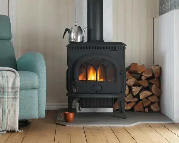 Mysig brasa i gjutjärnskamin med ved och tekopp. Tänk på renovera skorsten pris för en säker och effektiv värme.
