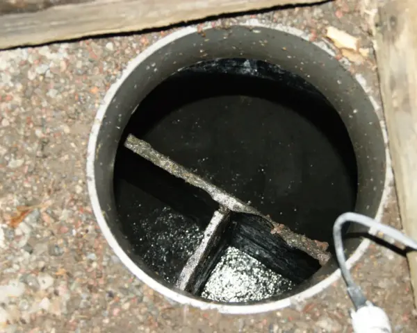 En gammal trekammarbrunn med mörkt vatten och en kabel som sticker in.