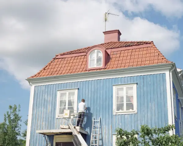 Man målar om en blå träfasad från en lift. En dropplist fasad skyddar mot regn.