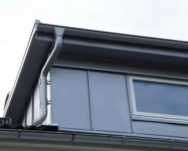 Grå takränna leder vatten från en stor takkupa med fönster.