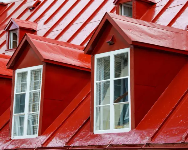 Två röda takkupor med vita fönster mot ett tak av olika typer av plåttak.