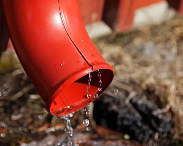 Rött stuprör leder bort smältvatten. Vatten droppar från mynningen ner mot marken, där det kan samlas i en stenkista avlopp.